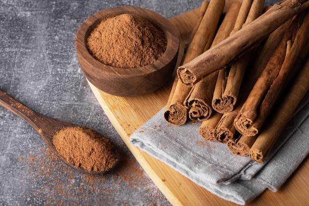 Foto canela em pó em uma tábua ao lado de uma tigela de madeira com canela em pó.