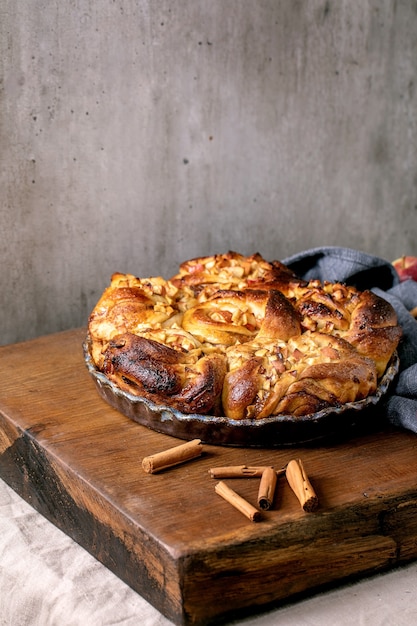 La canela pegajosa de la manzana dulce rueda los bollos en la bandeja para hornear redonda que se coloca con las manzanas que cultivan un huerto y los palitos de canela en la mesa de madera. Panadería casera tradicional. Copia espacio