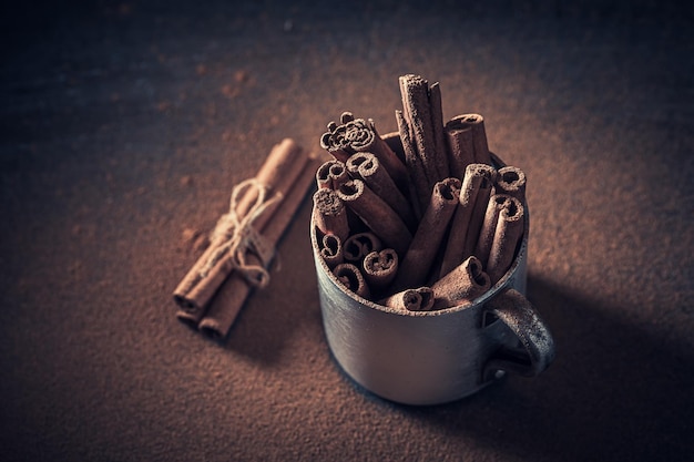 Canela en polvo y corteza en taza rústica sobre mesa oscura