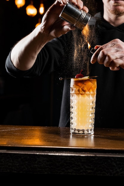 Canela queimando em um coquetel O barman derrama e o fogo queima a canela em um coquetel alcoólico em um bar O barman está preparando um coquetel alcoólico com uísque, xarope de açúcar com limão fresco e clara de ovo