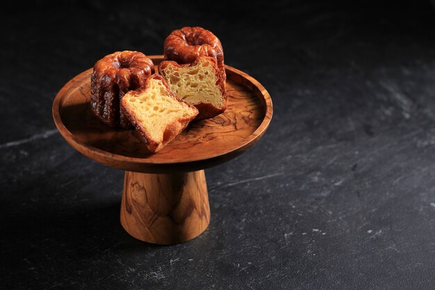 Canele Classic French Pastry Bordeaux en placa de soporte de pastel de madera, aislado sobre fondo de mármol negro. Copie el espacio para texto, receta, publicidad