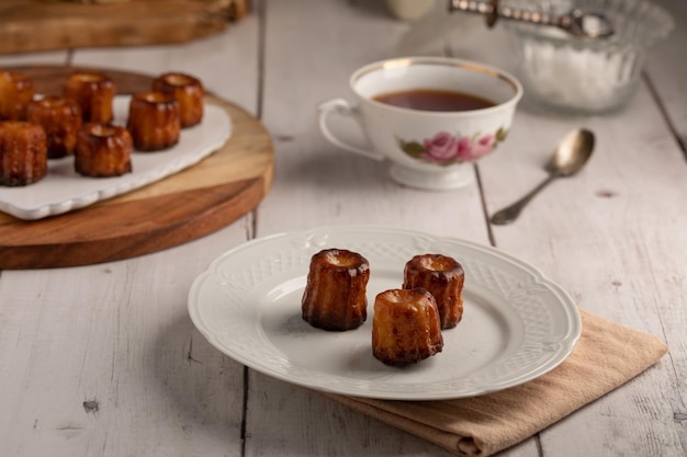 Caneles de Burdeos en un plato con té en una mesa de madera blanca