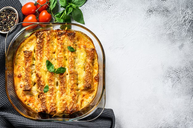 Foto canelone recheado com molho bechamel. macarrão cozido com carne, molho de natas, queijo. fundo cinza. vista do topo. copie o espaço