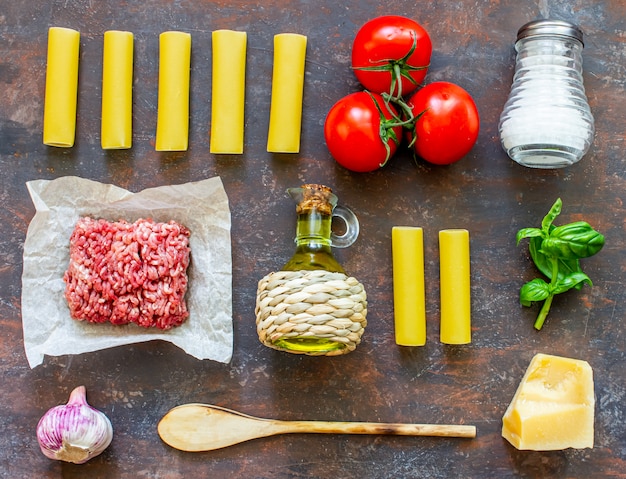 Canelone, tomate, carne picada e outros ingredientes. Fundo escuro. Cozinha italiana.