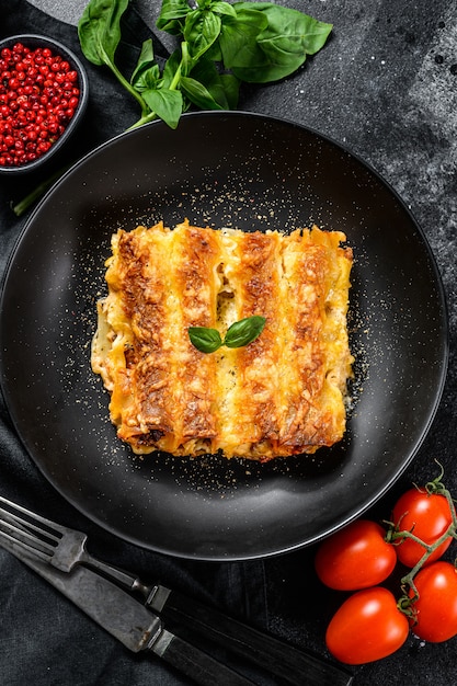 Canelones con carne y salsa de tomate. Pasta casera italiana. Fondo negro. vista superior