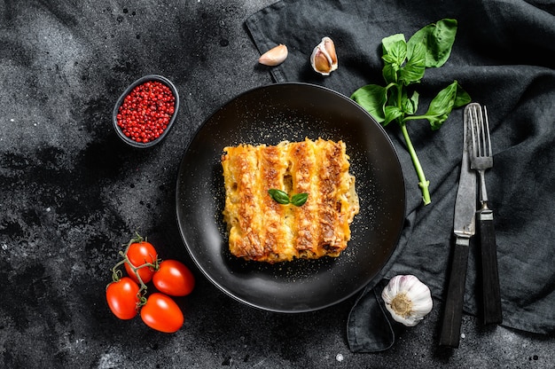 Canelones con carne y salsa de tomate. Pasta casera italiana. Fondo negro. vista superior