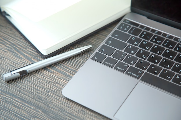 Caneta, caderno e caderno com teclado na mesa de madeira