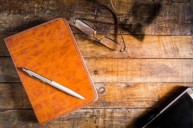 Caneta, caderno e smartphone no assoalho de madeira velho