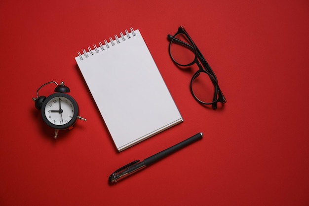 Caneta de bloco de notas de óculos despertador na mesa fundo vermelho espaço de texto seletivo