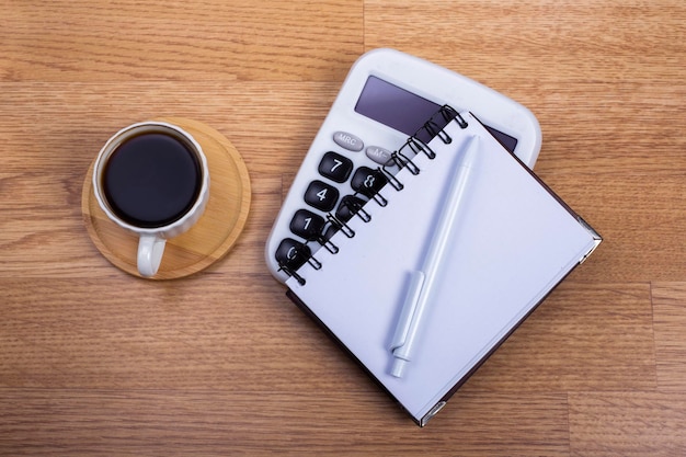 caneta de caderno e calculadora de café em fundo de madeira