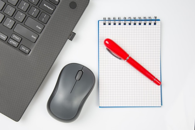 Foto caneta de mouse sem fio de computador e bloco de notas ao lado de um laptop em uma mesa branca closeup itens para trabalho de escritório