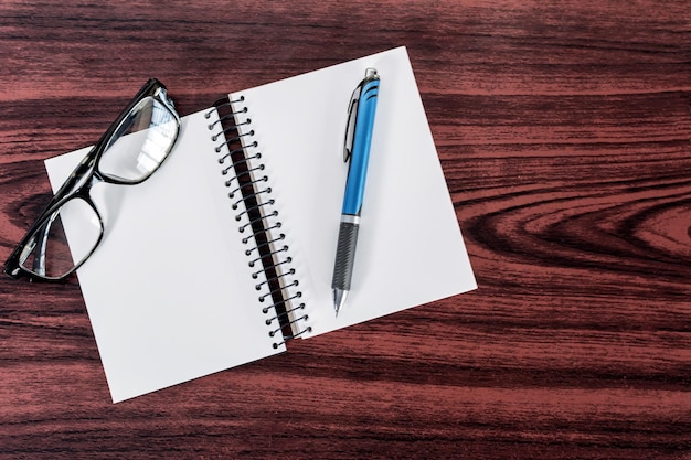 Caneta de notebook e óculos de leitura na mesa de madeira