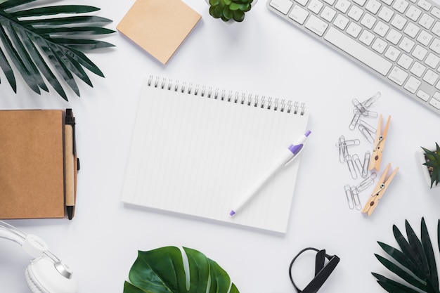 Caneta e bloco de notas em branco espiral rodeada de papelaria de escritório na mesa branca