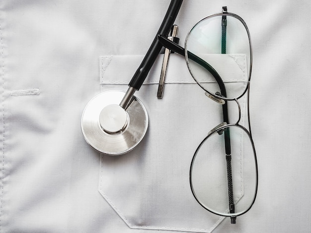 Caneta, estetoscópio, máscara facial e óculos, deitado em um vestido médico.