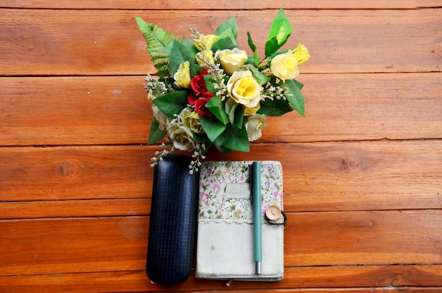 Caneta no caderno e óculos de óculos com flor de plástico na mesa de madeira