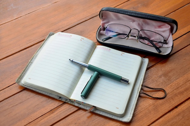 Caneta no caderno e óculos de óculos na mesa de madeira