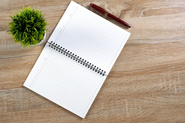 Caneta ou caneta de tinta com papel de caderno e pequena árvore de decoração em vaso branco na mesa de trabalho de madeira