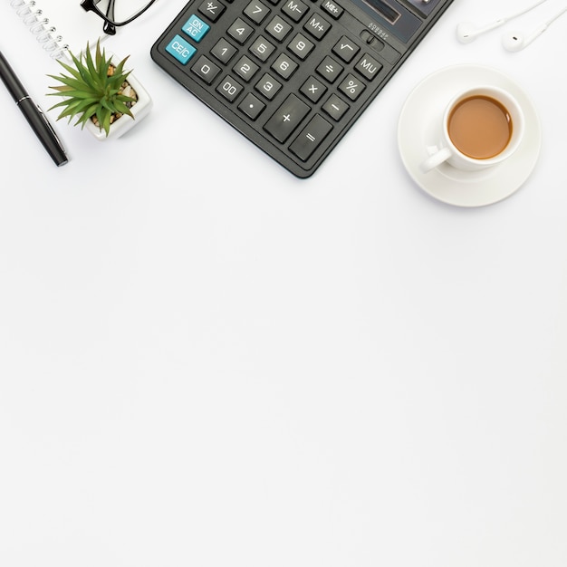 Foto caneta, planta do cacto, calculadora, fones de ouvido e xícara de café no fundo branco