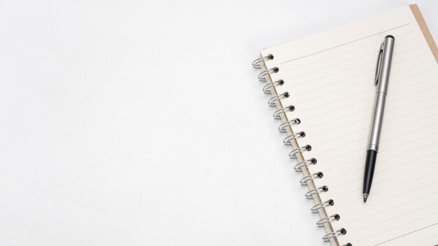 Caneta prateada e página em branco do caderno no espaço de cópia da vista superior da mesa