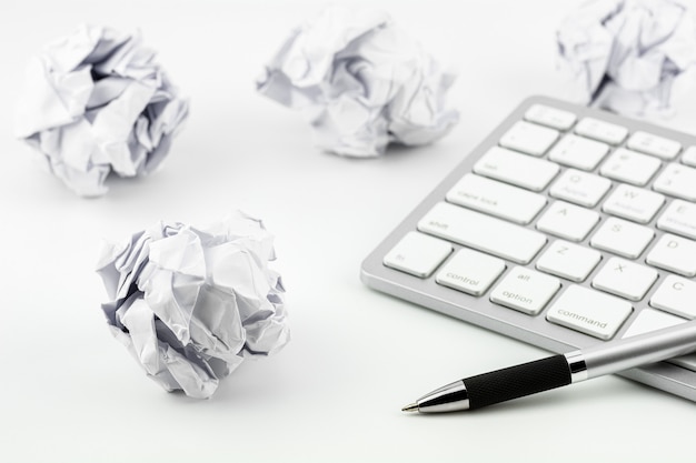 Canetas colocadas no teclado do computador e bolas de papel amassado em uma mesa branca