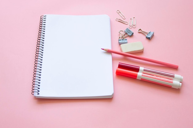 Canetas de feltro de lápis rosa e artigos de papelaria no bloco de notas com página em branco e fundo rosa