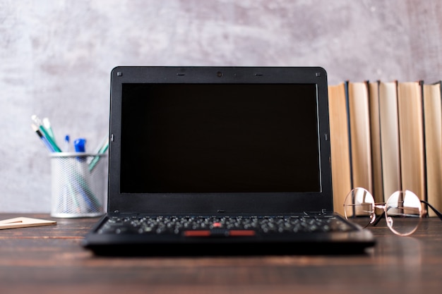 Canetas, maçã, lápis, livros, laptop e óculos em cima da mesa, no fundo do quadro-negro