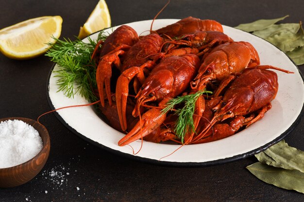 Foto cangrejo de río rojo con eneldo, laurel y limón en un plato.