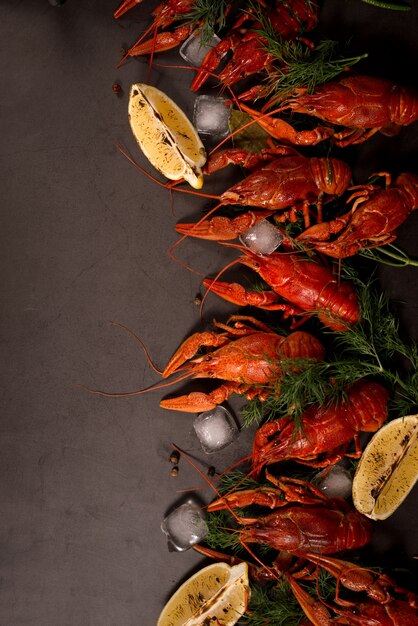 Cangrejo rojo hervido listo para comer con rodajas de limón y cubitos de hielo sobre una superficie negra