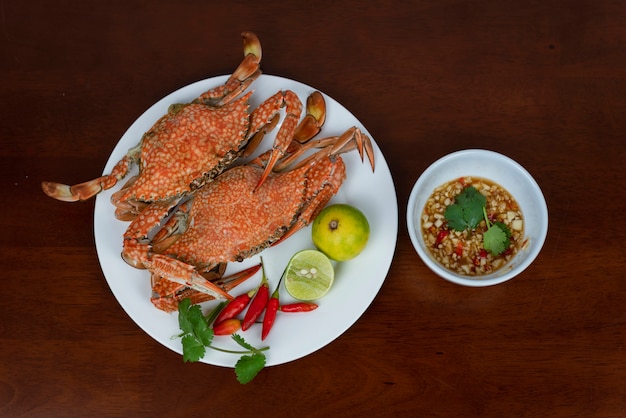 Cangrejos azules con la salsa de inmersión tailandesa de los mariscos en una placa, en un fondo de madera