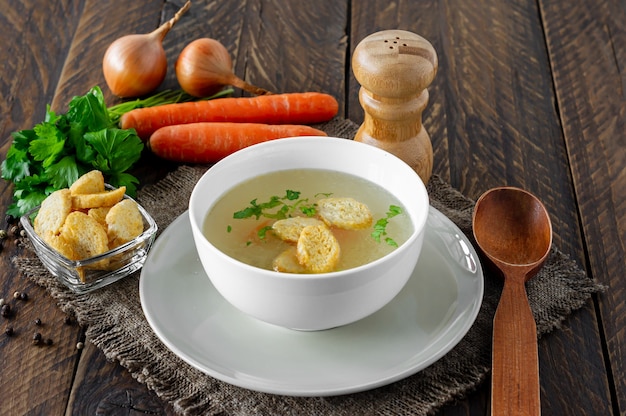 Canja de galinha com legumes em uma tigela branca. Saboroso caldo caseiro em um fundo de madeira.