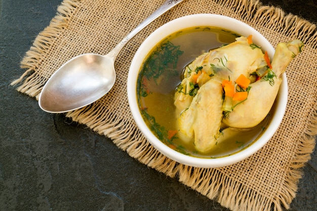 Canja de galinha com vegetais em um fundo preto.