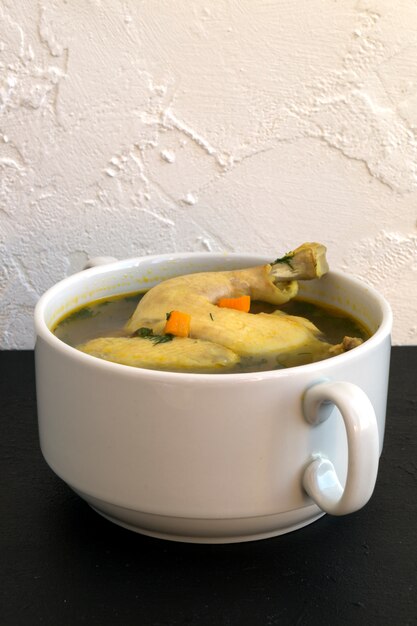 Canja de galinha com vegetais em um fundo preto.