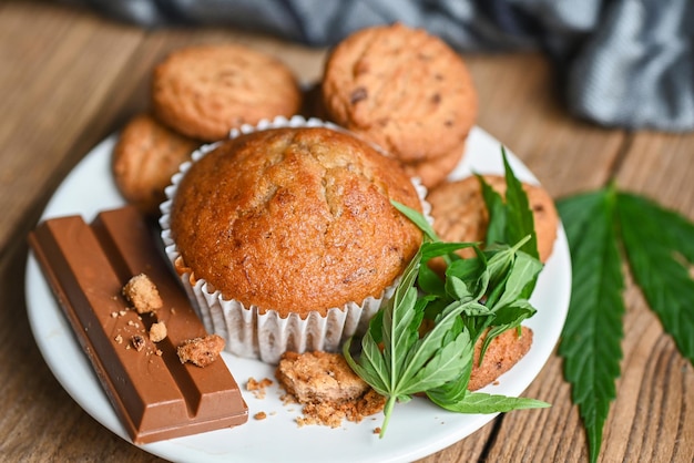 Cannabis-Lebensmittelkekse mit Kuchenschokoladen-Cannabisblatt-Marihuana-Kraut auf hölzernem und dunklem Hintergrund, köstlicher süßer Dessert-Keks mit Hanfblattpflanze THC CBD-Kräuter-Nahrungssnack und medizinischer Draufsicht