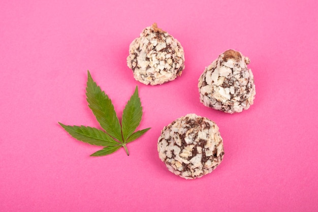 Cannabis-Süßigkeiten, Schokoladentrüffel-Bonbons mit Nüssen und grünem Marihuana-Blatt auf rosa Hintergrund.