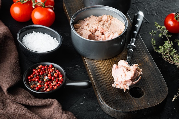 Canned Chunk Light Thunfisch auf Holzbrett auf schwarzem Hintergrund mit Kräutern und Zutaten