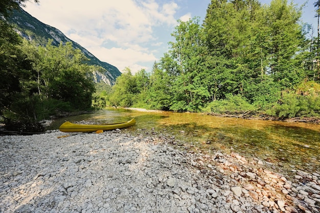 Una canoa amarilla descansa sobre una orilla rocosa de un tranquilo lago azul en el Parque Nacional Triglav Eslovenia
