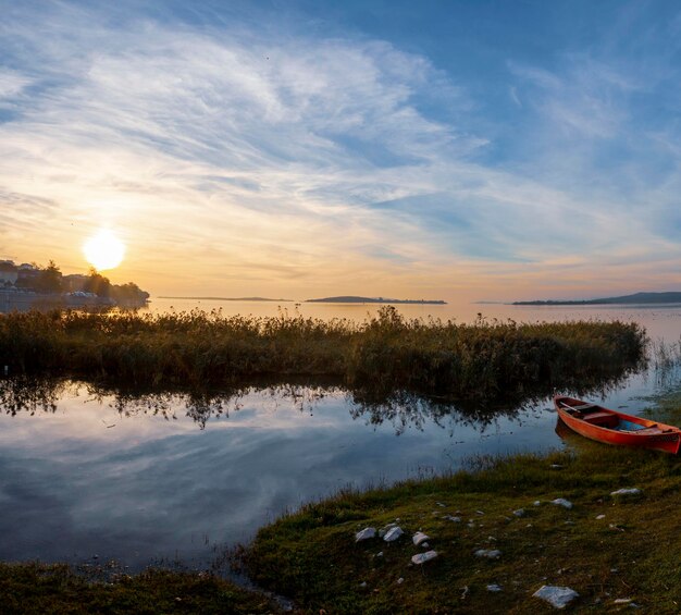 Foto una canoa roja está en la orilla de un lago con el sol poniéndose detrás de ella