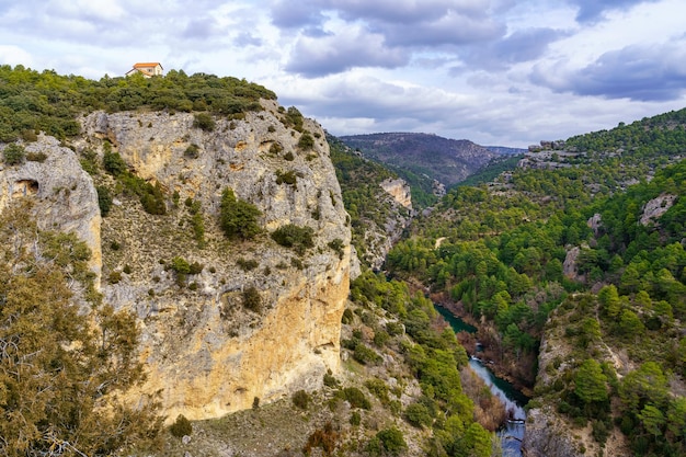 Cañón de roca en el bosque con una pequeña casa en lo alto del acantilado