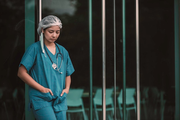 Cansada, deprimida, asiática, enfermera de cirugía, usa máscara facial, uniforme azul, se sienta en el suelo del hospital, mujer joven, doctora, estresada por el trabajo duro.