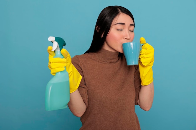 Cansada e exausta jovem dona de casa asiática tomando café durante o intervalo do trabalho enquanto segura uma esponja por outro lado, Limpando o conceito de casa, Chá de refresco descansa um pouco das tarefas do dia a dia,