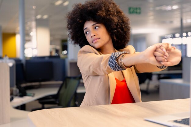 Foto cansada jovem empresária afro-americana com penteado afro, esticando as mãos no local de trabalho