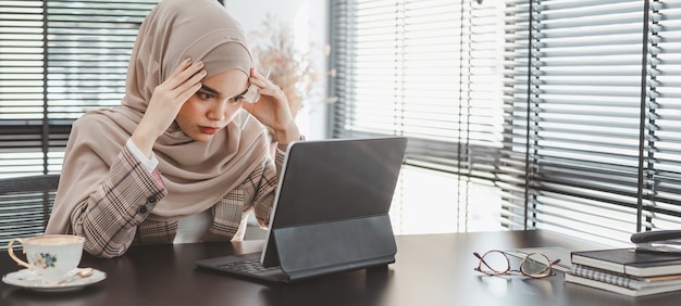 Cansado e frustrado jovem muçulmano mulher de negócios marrom hijab se sentindo estressado segurando a cabeça com as mãos, conceito de falha de problema de negócios