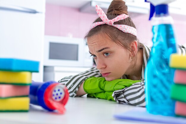 Cansado, con exceso de trabajo, triste ama de casa con guantes de goma protectores descansando de limpiar la casa.