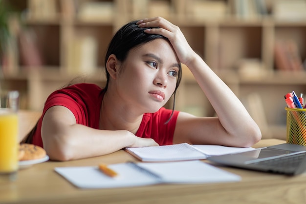 Cansado frustrado e chato adolescente estudante asiática estuda em casa olha para laptop no interior do quarto