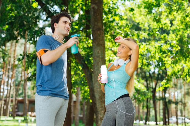 Cansado de hacer ejercicio. Mujer joven positiva sosteniendo su mano mientras está de pie con su novio después de un entrenamiento