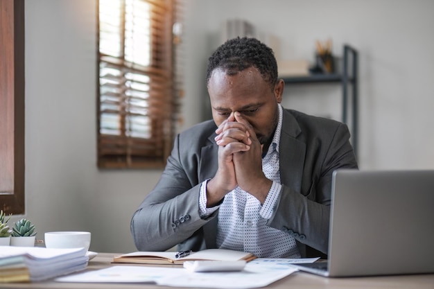 Cansado hombre de negocios africano con los ojos cerrados sentado estrés en su escritorio en la oficina
