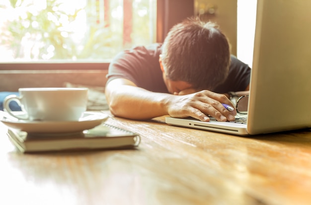 Cansado homem asiático com a cabeça para baixo no laptop computador enquanto trabalhava.