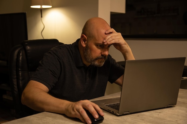 Cansado homem de meia idade brasileiro usando um laptop trabalhando em casa à noite