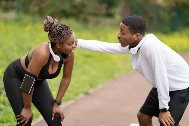 Cansado jovem casal afro-americano alegre em roupas esportivas descansando depois de correr no parque