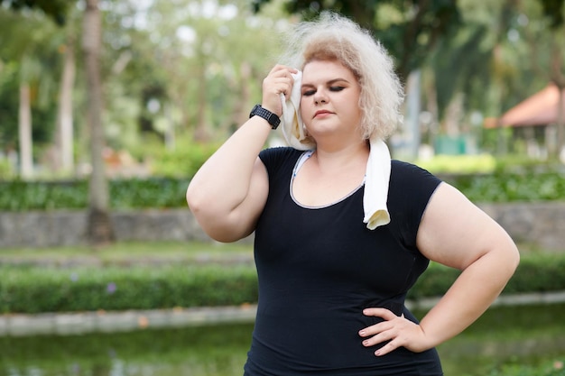 Cansado jovem curvilíneo limpando o suor da testa depois de correr no parque